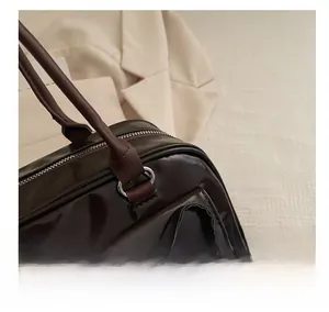 Detailed close-up of dark brown patent leather handbag with silver metal ring and bow detail