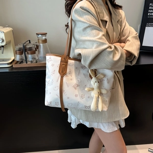 White tote bag with brown leather straps and cartoon print shown in a cafe setting