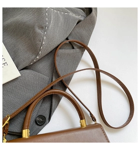 Detail of brown leather bag with retro handle on grey blazer with white stitching