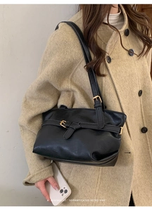 Dettaglio della borsa tote minimalista in pelle nera con fibbia indossata sulla spalla
