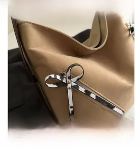 Détail du sac fourre-tout en daim beige avec zip diagonal et ruban à nœud à pois noirs