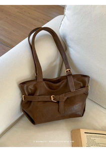 Detail of dark brown leather tote bag with buckle straps on a white sofa in a cozy home setting