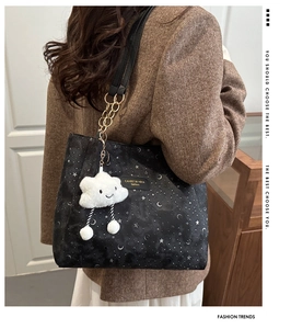 Detail of black tote bag featuring moon and star patterns and a plush cloud charm
