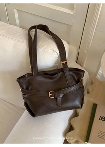 Detail of a vintage dark brown tote bag with gold buckle on a soft white fabric sofa