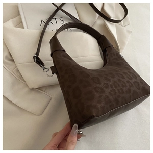Detail view of vintage leopard print crescent hobo bag resting on a white suit and book