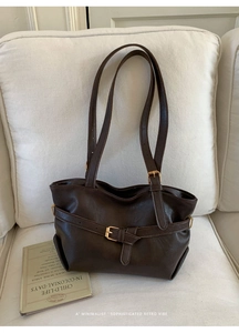 Detail of a dark brown retro tote bag with a golden buckle on a soft white sofa