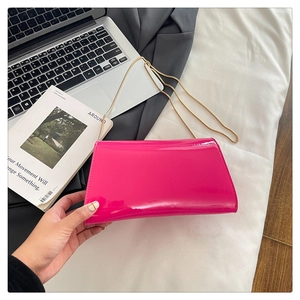 Trendige pinke Lackleder-Umschlagtasche mit goldener Kette auf weißem Laken dekoriert
