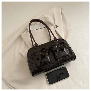 Detail of a shiny dark coffee brown tote bag with cute bow accents and flip pockets