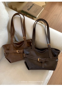 Detail view of brown vintage leather tote bags with metal buckle straps on white sofa