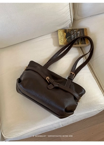 Detail of dark brown vintage tote bag with gold buckle on a minimalist white sofa