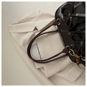 Detail of dark brown glossy Boston bag featuring decorative bows and wooden bead charm