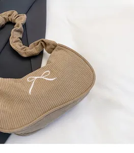 Dettaglio borsa baguette in velluto a coste kaki con fiocco ricamato e tracolla arricciata