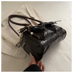 Detail of dark brown glossy shoulder bag with front flap pockets and wooden bead charm