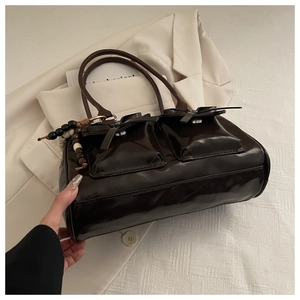 Detail of dark brown glossy leather handbag with front pockets and bead charm