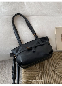 Detail of black glossy leather tote bag featuring elegant golden buckle and strap accents