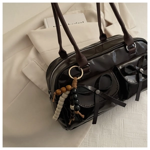 Detail of dark brown polished shoulder bag featuring bow accents and beaded charm