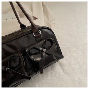 Close-up of a glossy dark brown leather bag with a bow knot and silver metal rings