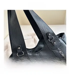 Detail of black leather tote bag featuring metallic rivets and side zipper accents