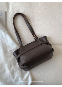 Detail view of large brown leather tote bag with side pleats and golden metal buckle
