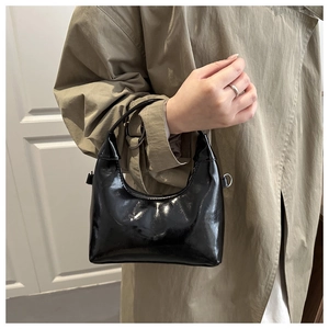 Borsa hobo nera lucida in vernice portata da una modella con un trench beige