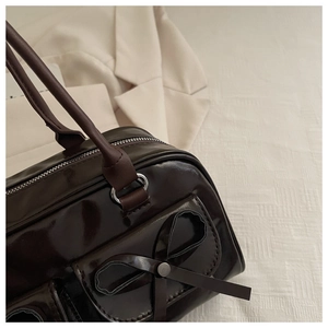 Close-up of brown patent leather handbag featuring bow detail and silver metal hardware