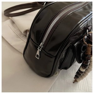 Detail of glossy dark brown leather bag with silver zipper and beaded charm accent