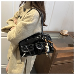 Detail of black glossy shoulder bag with bow pockets and wooden bead pendant accessory