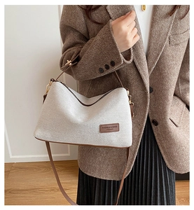 Detail of beige canvas shoulder bag with brown leather trim and embossed fashion logo