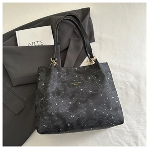 Detail of black tote bag featuring silver star and moon patterns and leather label logo