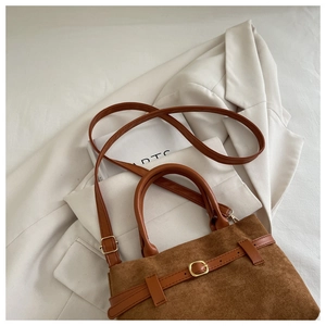 Detail of a brown matte suede handbag with gold buckle on a minimalist lifestyle background