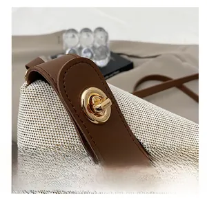 Close-up of golden metal turn-lock on woven cream shoulder bag with brown leather trim