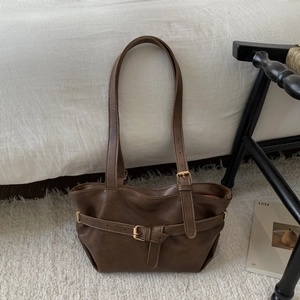 Deep brown minimalist tote bag with metal buckle detail on a white plush carpet