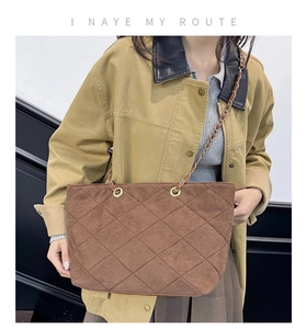 Close-up of brown quilted suede tote bag with metal chain strap on model