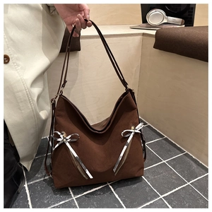 Detail of dark brown tote bag with silver bow ribbon and zipper in a lifestyle setting