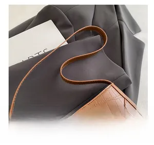 Detail of caramel crocodile embossed leather handbag with metal rivets on a grey blazer