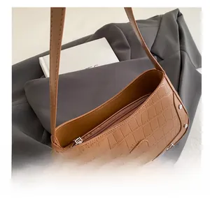 Detail view of smooth top zipper and brown crocodile texture on crescent bag with heart patch