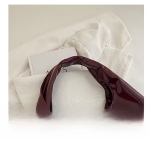 Top view of wine red patent leather tote bag with wide strap on a soft textured fabric