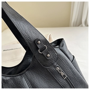 Detail of black lychee grain leather handbag with metal zipper and rivet accents