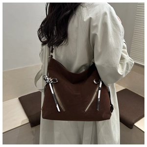 Detail of dark brown tote bag featuring decorative silver zippers and ribbon tassels