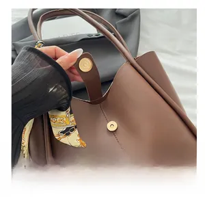 Close-up of brown leather tote bag featuring magnetic metal buckle and decorative silk scarf