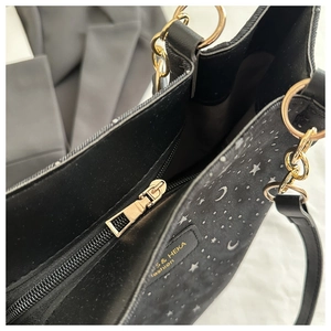 Detail view of black tote bag showing gold zipper, star moon prints and fabric texture