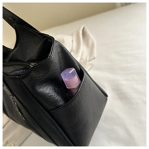 Detail view of the black leather tote showing a side pocket with a small perfume bottle