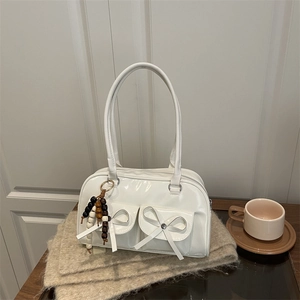 White glossy bow hobo bag with wooden bead charm on a cozy knit blanket