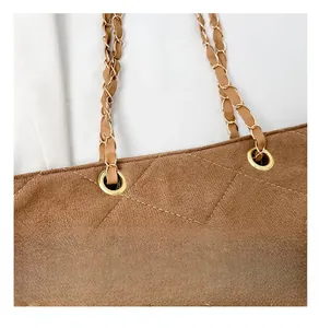 Detail of brown quilted suede tote bag featuring gold chain strap and metal eyelets