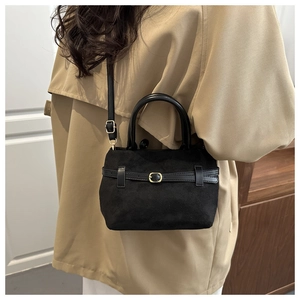 Détail du sac seau noir en daim mat avec boucle dorée et bandoulière porté par un mannequin