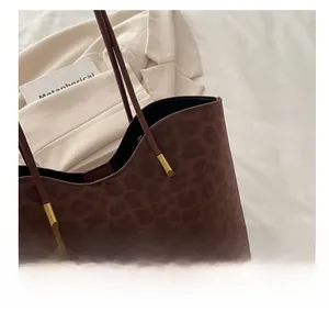 Detail showing brown leopard print tote bag with gold metal buckle on white suit