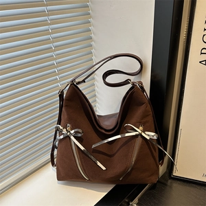 Brown tote bag with ribbon bows and dual zippers on a window sill with light shadows