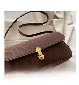 Detail of a brown faux suede bag with a large gold oval lock on a white blazer