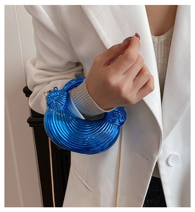 Detail of blue crescent acrylic bag with striped texture and gold chain on white blazer