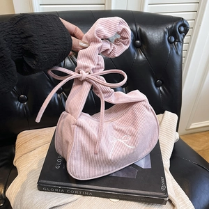 Sac demi-lune en velours rose avec broderie nœud et poignée froncée sur canapé noir